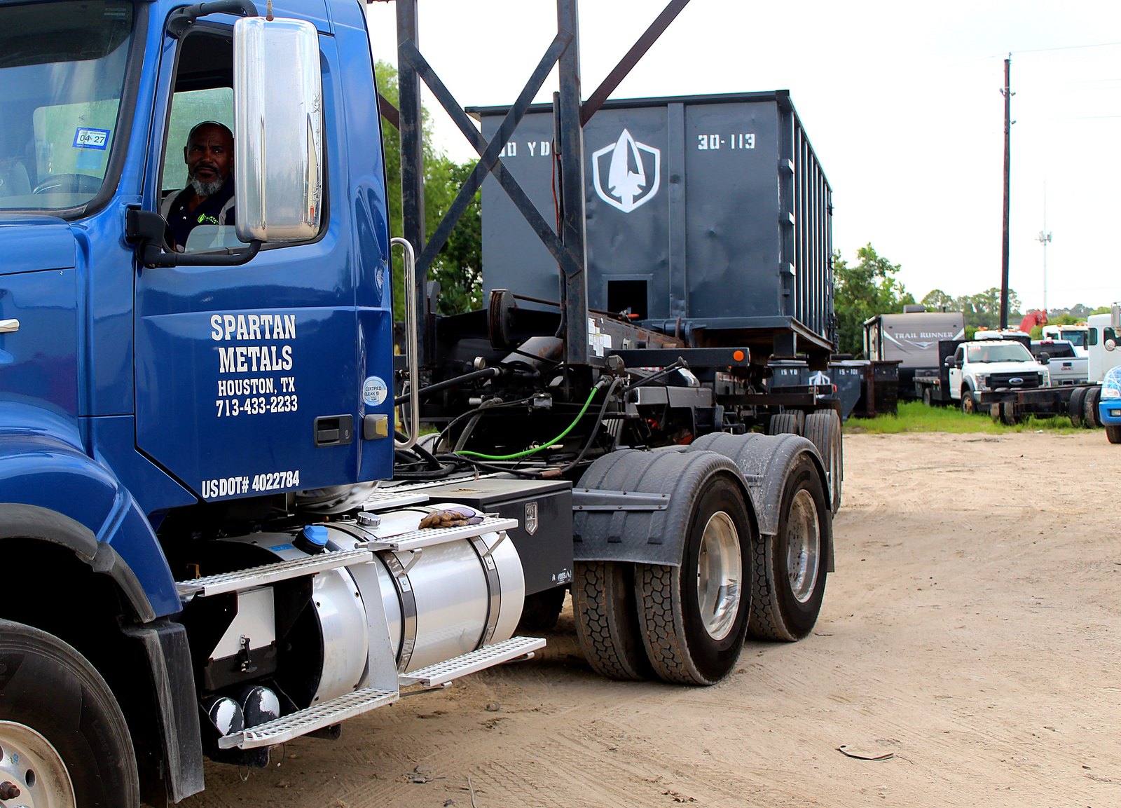Spartan Metals blue roll-off truck with driver at the wheel in the Houston yard